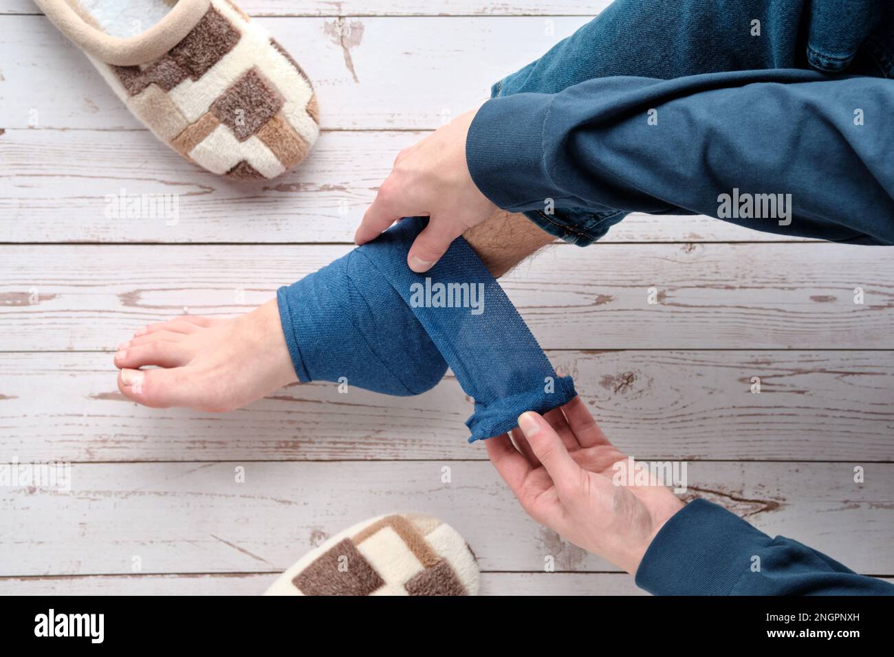 Teenage boy wrapping compression bandage around sprained ankle to