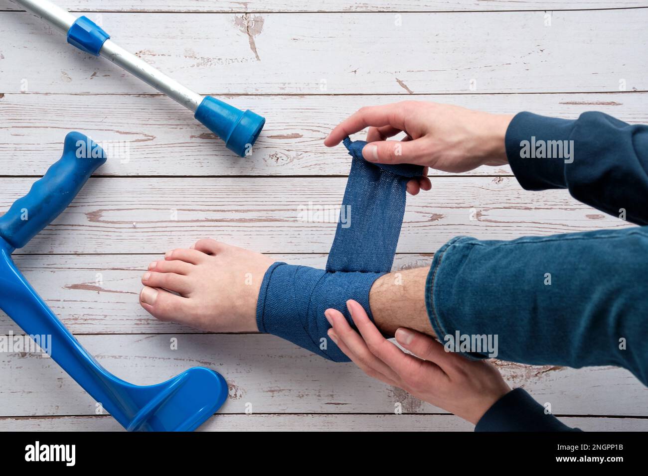 Teenage boy wrapping compression bandage around sprained ankle to