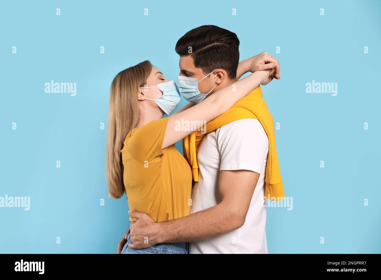Couple in medical masks trying to kiss on light blue background Stock ...