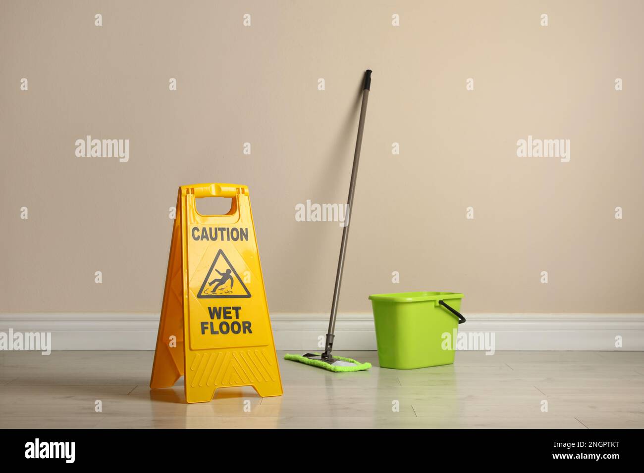 Safety sign with phrase Caution wet floor, mop and bucket indoors