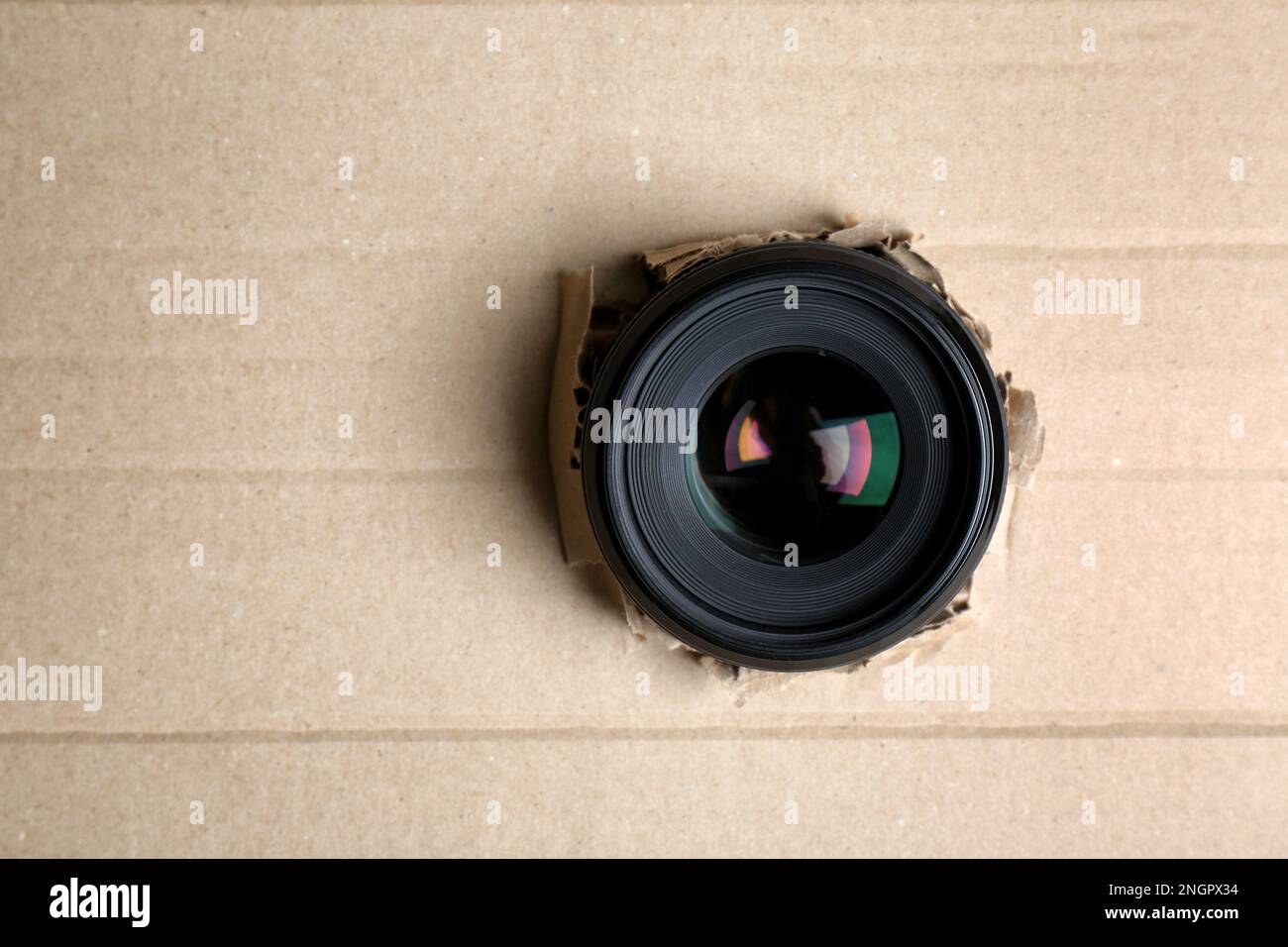 Hidden camera lens through hole in cardboard. Space for text Stock