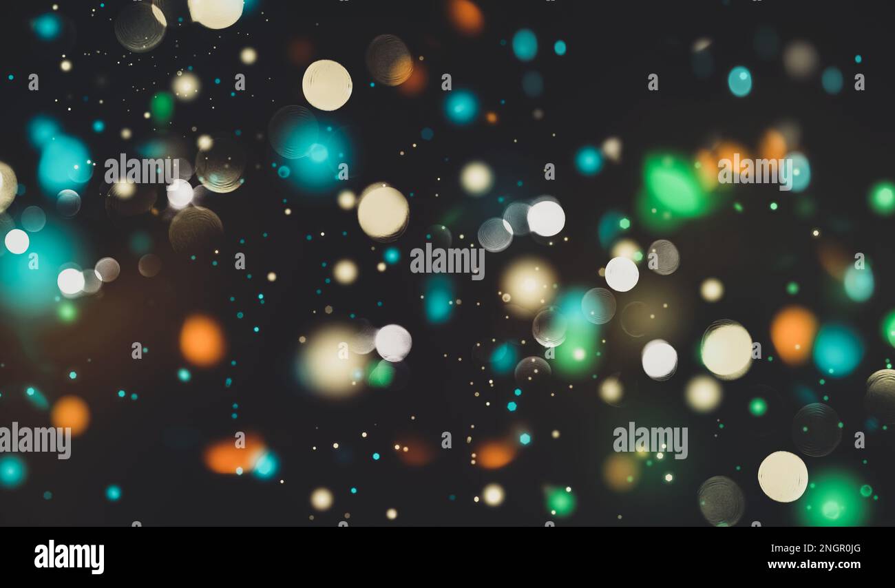 Flying particles on black background, bokeh texture, blurred festive lights, glittering confetti burst out, shiny speckles, orange green blue white co Stock Photo