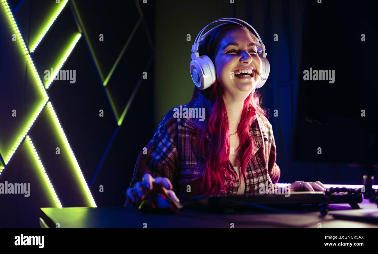 Woman sitting at her gaming station with a headset, laughing in celebration of her latest victory in an online game. Female gamer enjoying herself as Stock Photo
