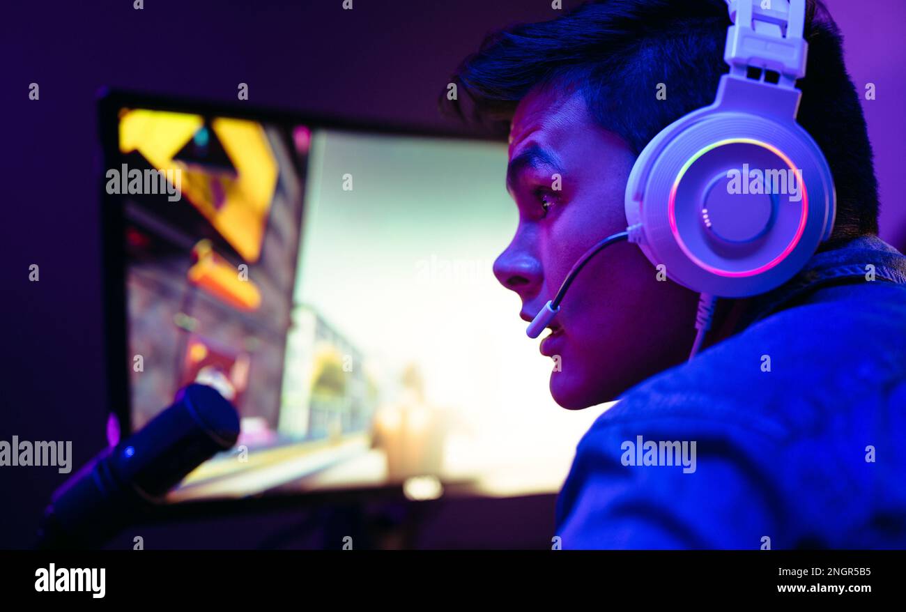 With a computer in front of him, a video game player live streams his gameplay. With his headset and microphone, he enters into the world of online vi Stock Photo