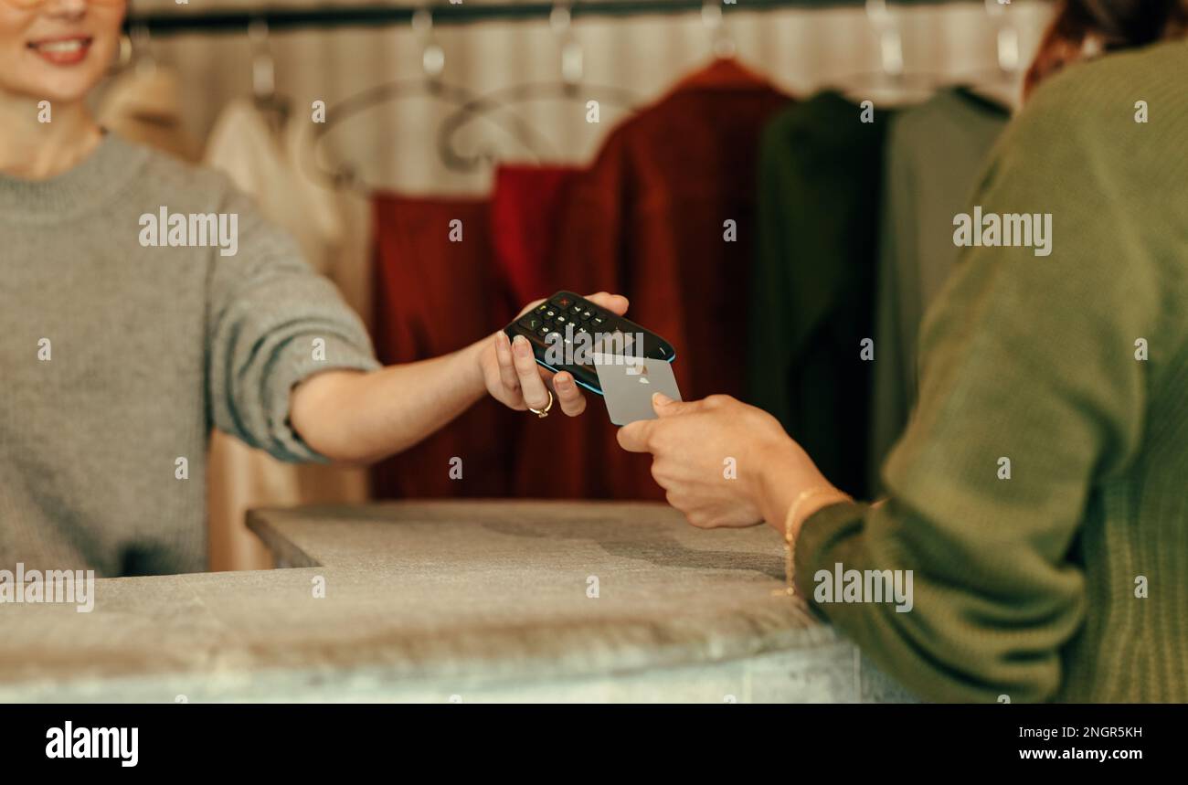 Unrecognisable female customer paying with a credit card at the checkout counter. Young woman tapping a credit card on a contactless card reader. Woma Stock Photo