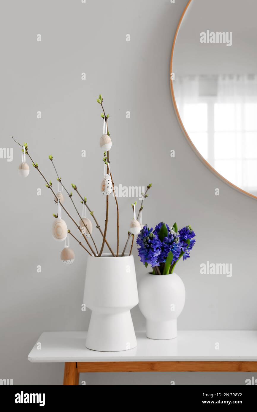 Vases with tree branches, Easter eggs and flowers on table in room ...