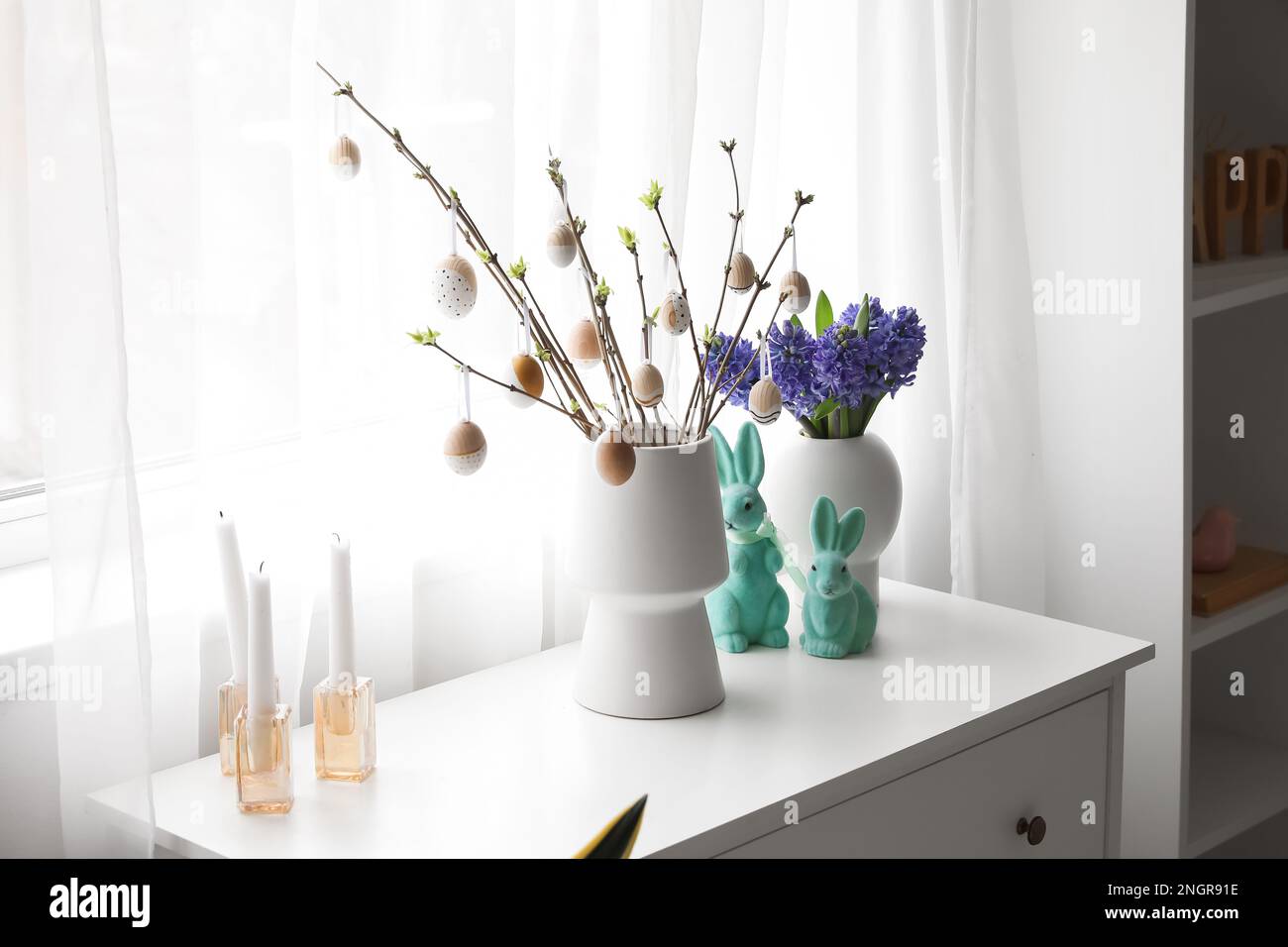 Vases with tree branches, Easter eggs, flowers and rabbits on chest of ...
