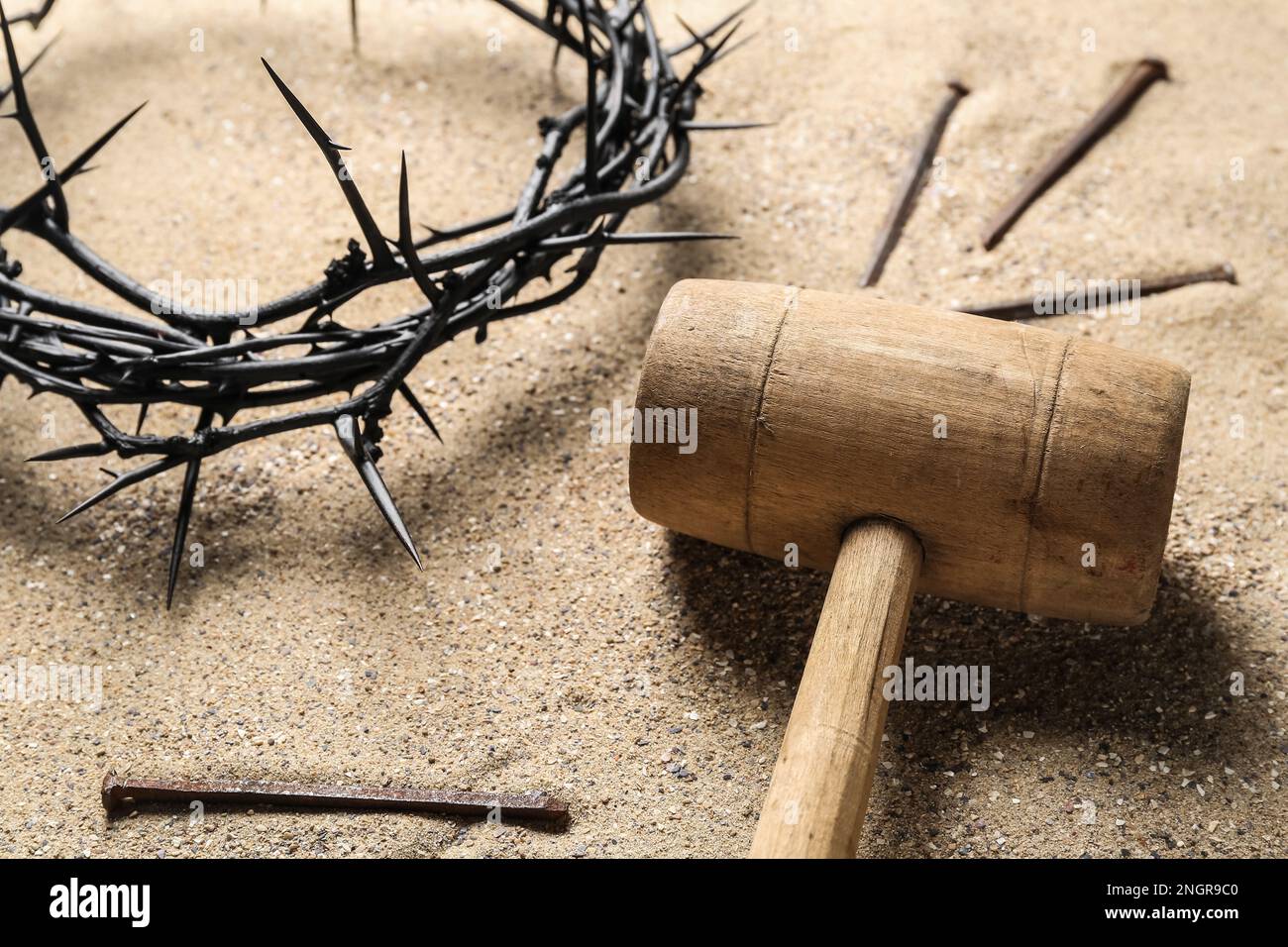 Mallet with crown of thorns and nails on sand, closeup. Good Friday