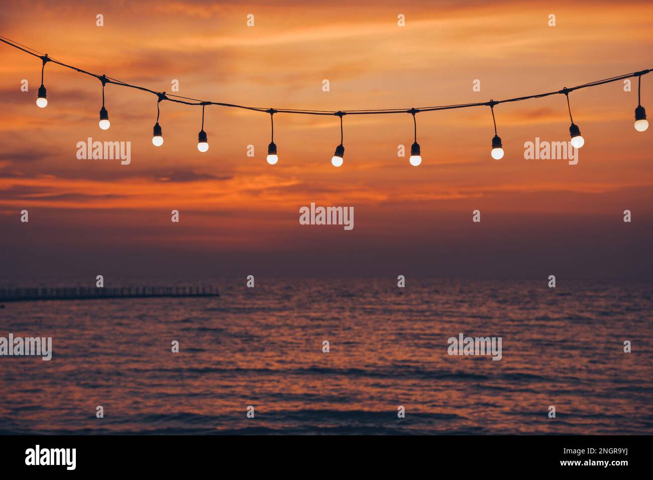 light bulbs on string wire against sunset sky by the beach Stock Photo