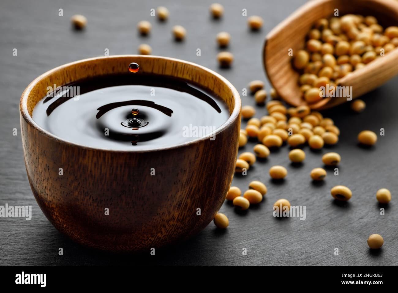 soy sauce with spalsh and drop in wooden bowl and dry soybeans in scoop Stock Photo