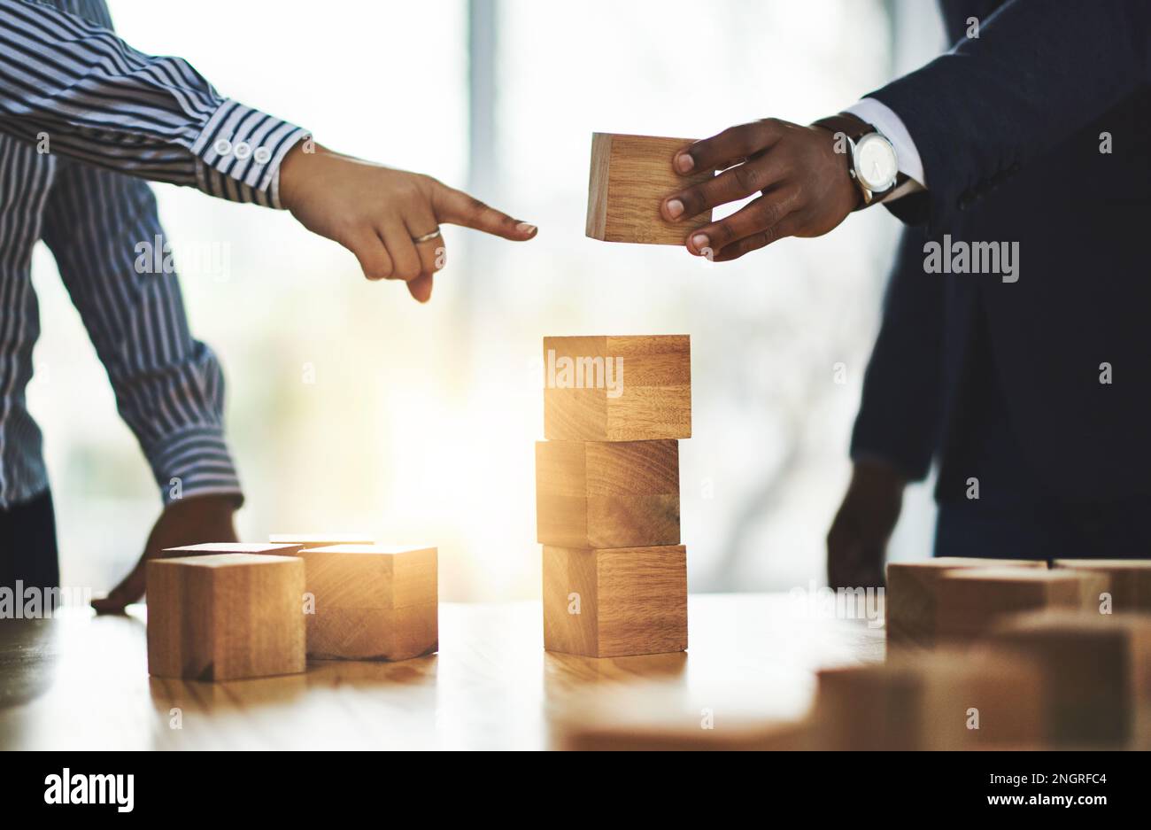 Working in synergy to overcome all obstacles in their way. two businesspeople stacking wooden blocks together in an office. Stock Photo