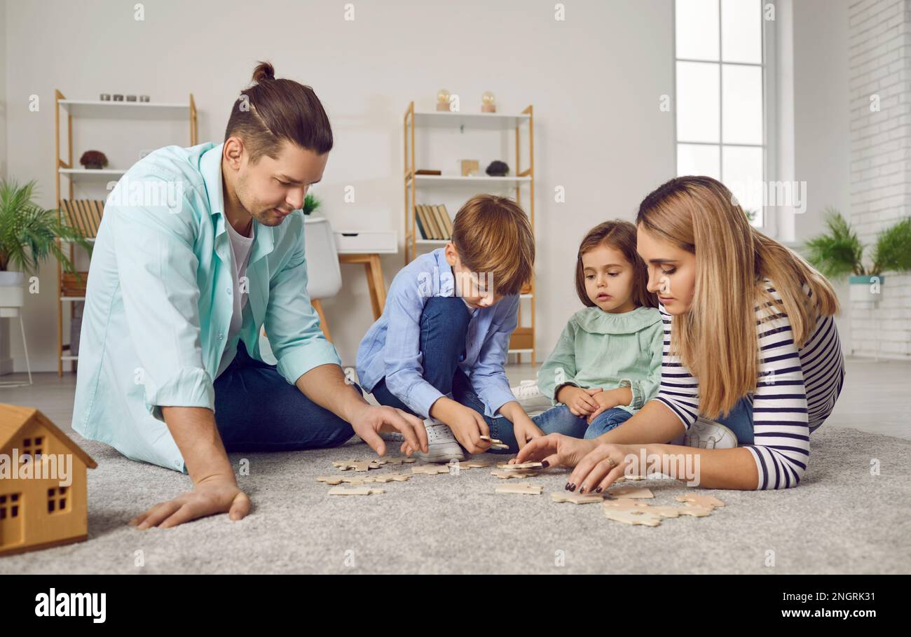 Parents playing with two kids in a puzzle on the floor in the living room at home. Stock Photo