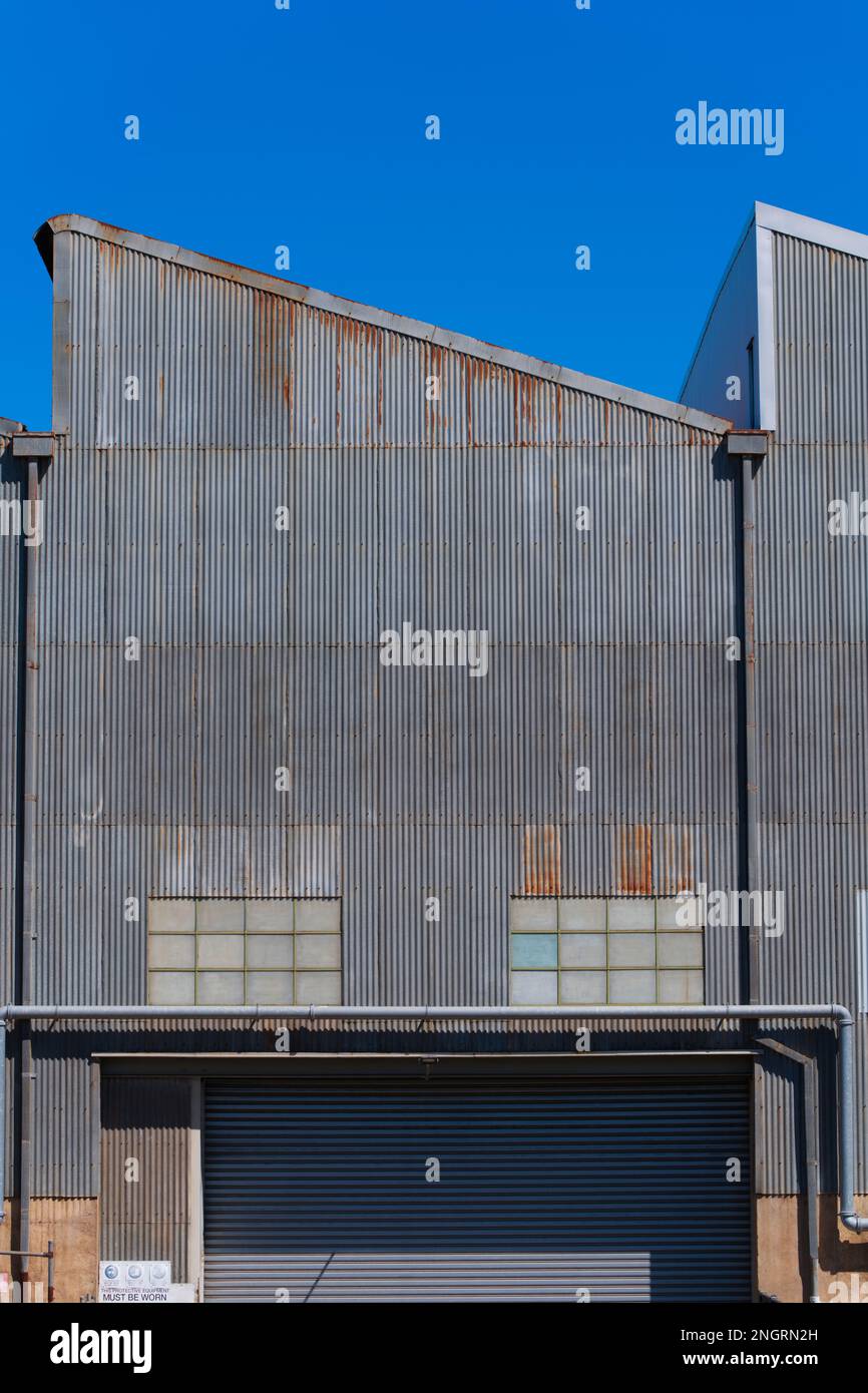 Metal corrugated iron factory wall, windows and entry with a cloudless blue sky in Castlemaine Australia. Stock Photo