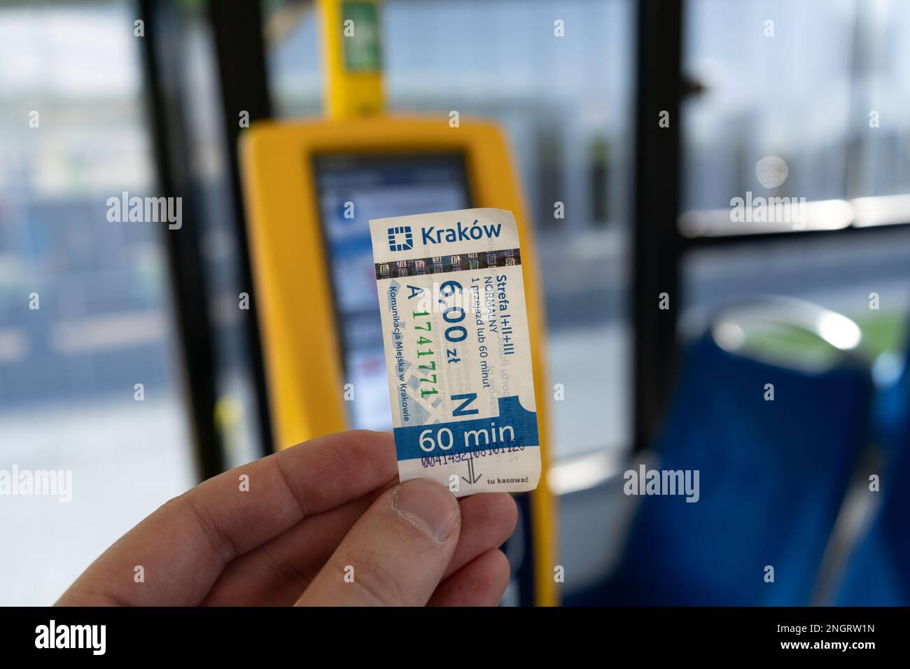 Hand holding a 60-minute full fare ticket type inside a MPK Kraków public transport bus, next to validation machine in Krakow, Poland. Stock Photo