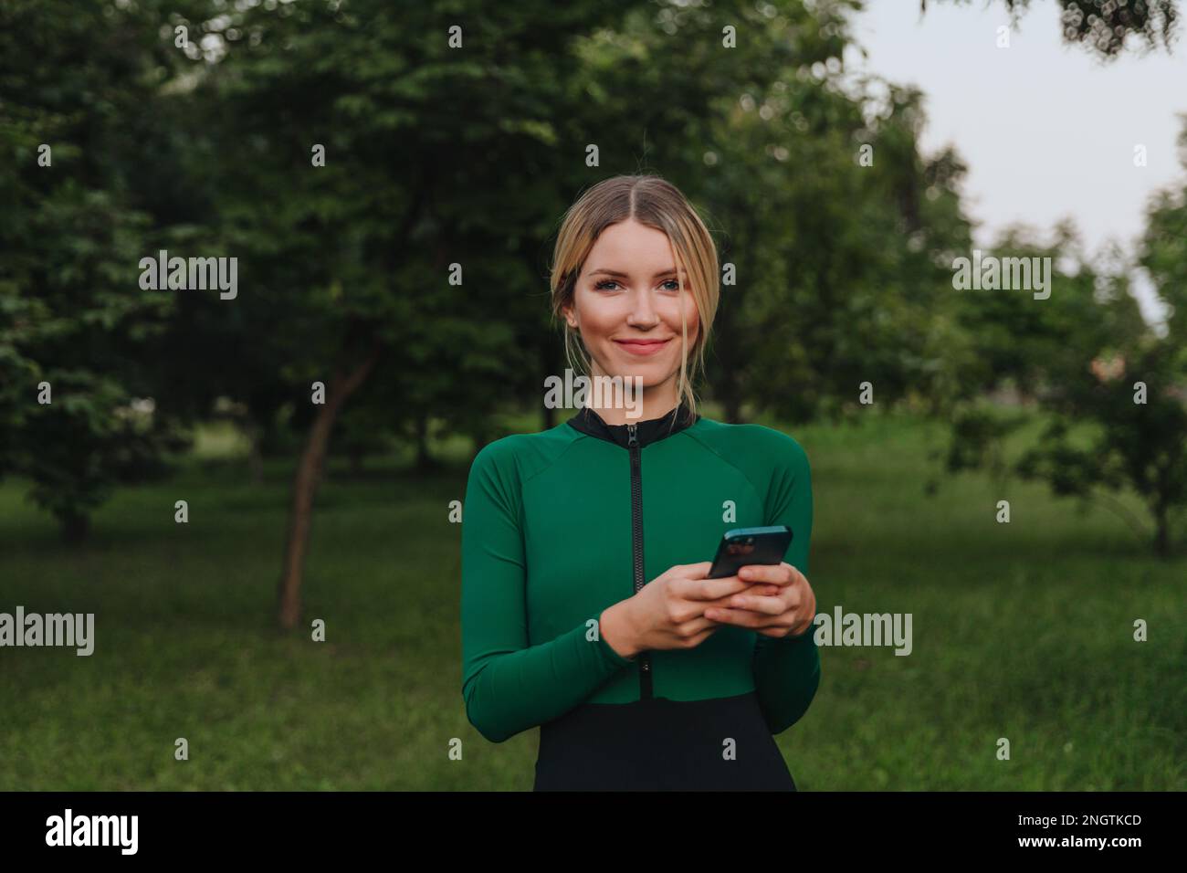 Yoga in the park with sunlight. A young woman in a lotus position sits on green grass and using cell phone. The concept of digital transformation. Stock Photo