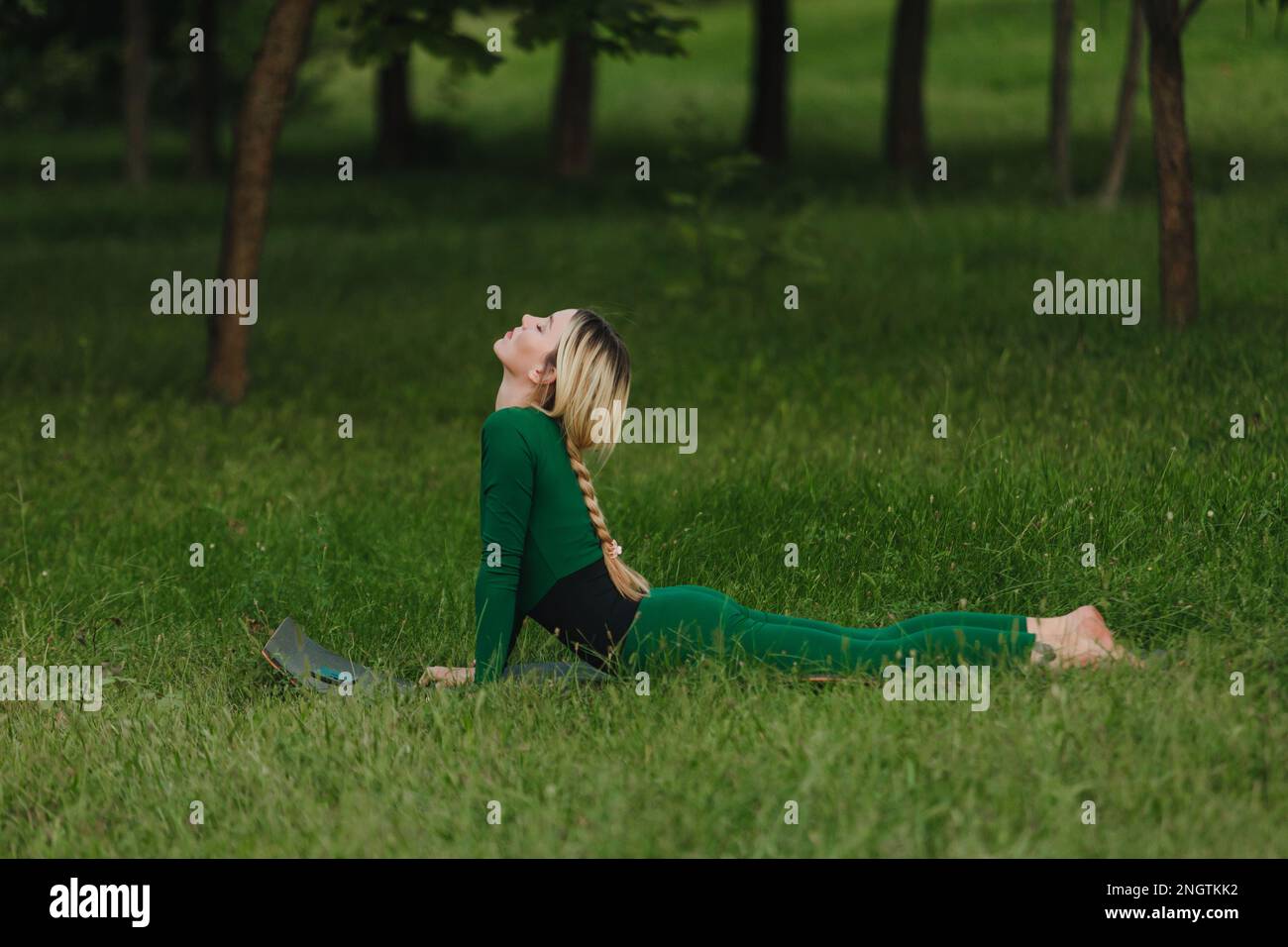 A young beautiful girl is doing yoga in a calm warm evening on the grass. Stock Photo