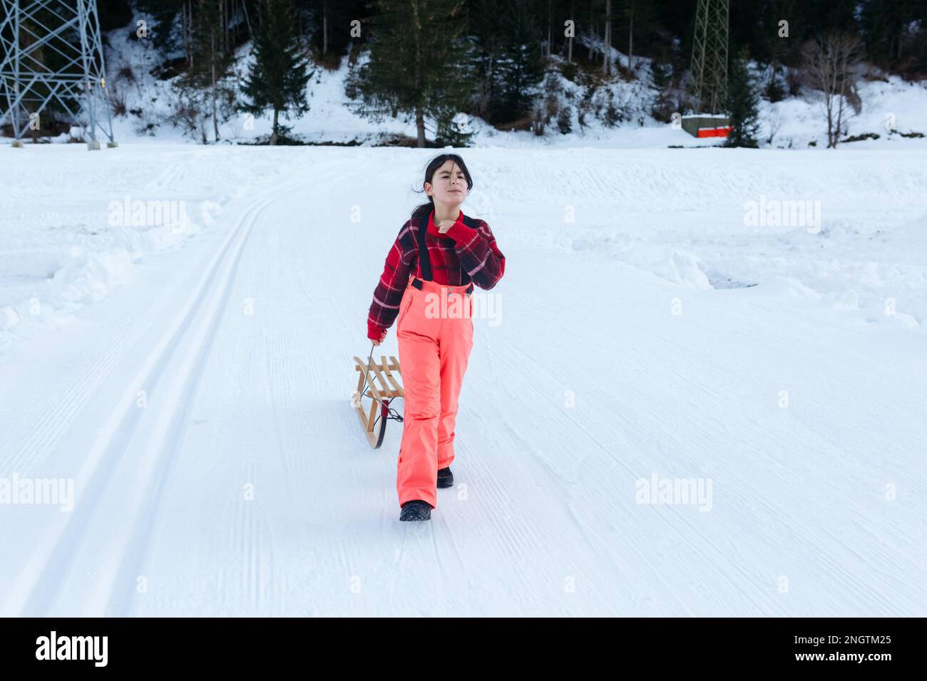 girl in red pullover and orange ski pants walk up with wooden sled