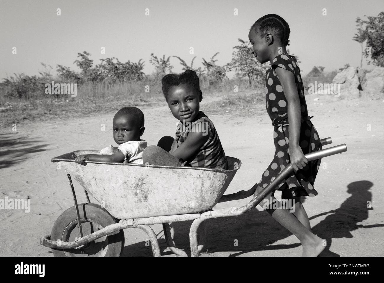Young girl pushing her friends in a wheelbarrow in rural Africa Stock ...