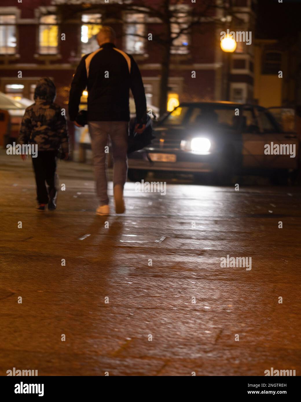 Blurred defocused father and son crossing a pedestrian street at night. Car with lights driving around them Stock Photo