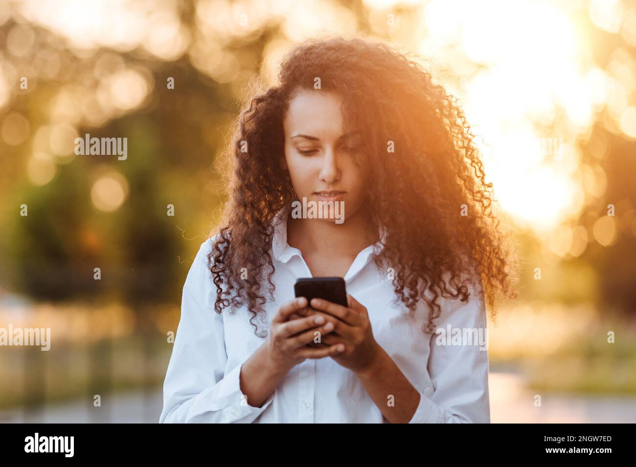 A young girl walks in the park and uses social networks using a mobile phone. Stock Photo