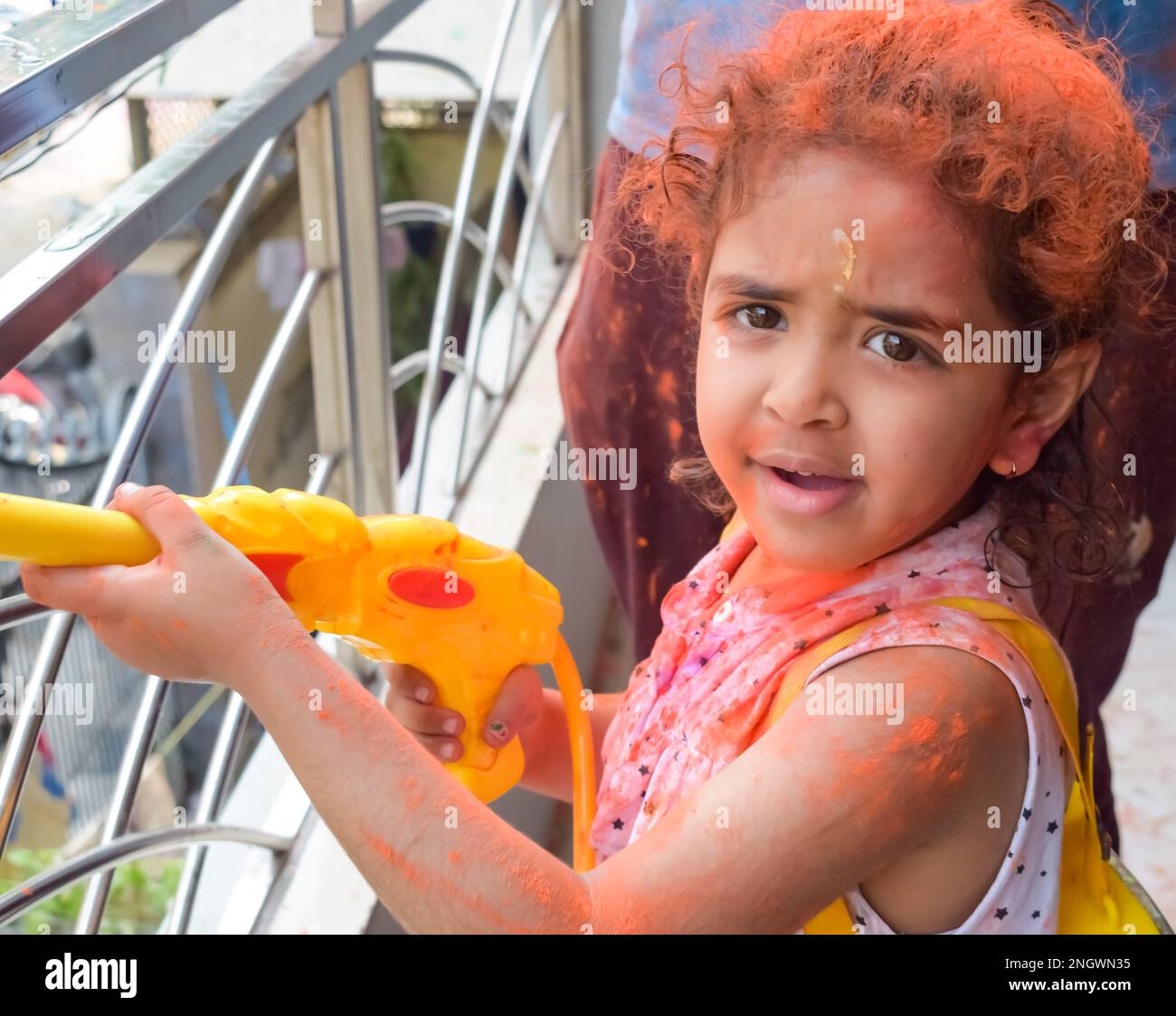 Sweet little Indian girl playing colours on Holi festival, holding pichakaree full of colours, Holi festival celebrations in Delhi, India. Stock Photo