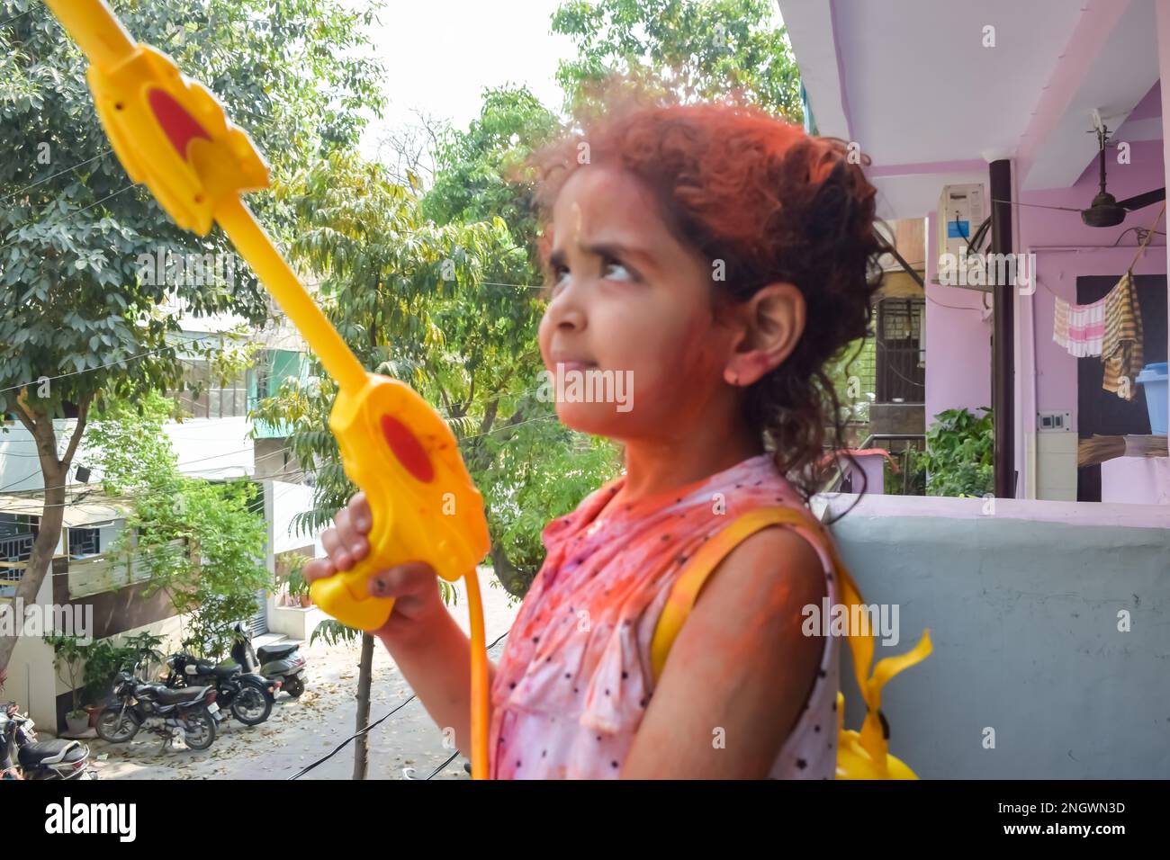 Sweet little Indian girl playing colours on Holi festival, holding pichakaree full of colours, Holi festival celebrations in Delhi, India. Stock Photo