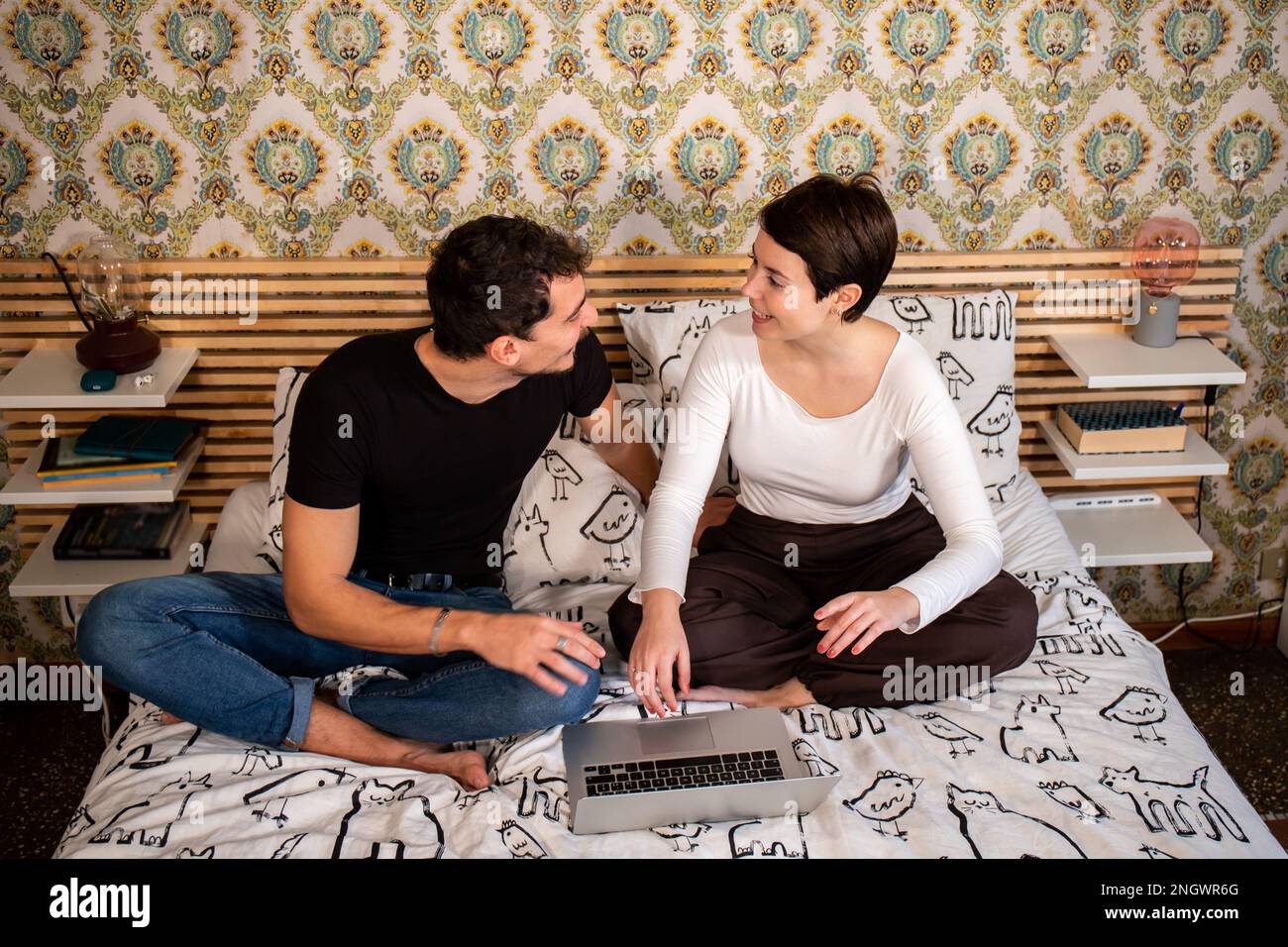 Young couple is sitting on the bed and using the computer. The couple are planning a home renovation. Concept of love and happiness. Stock Photo