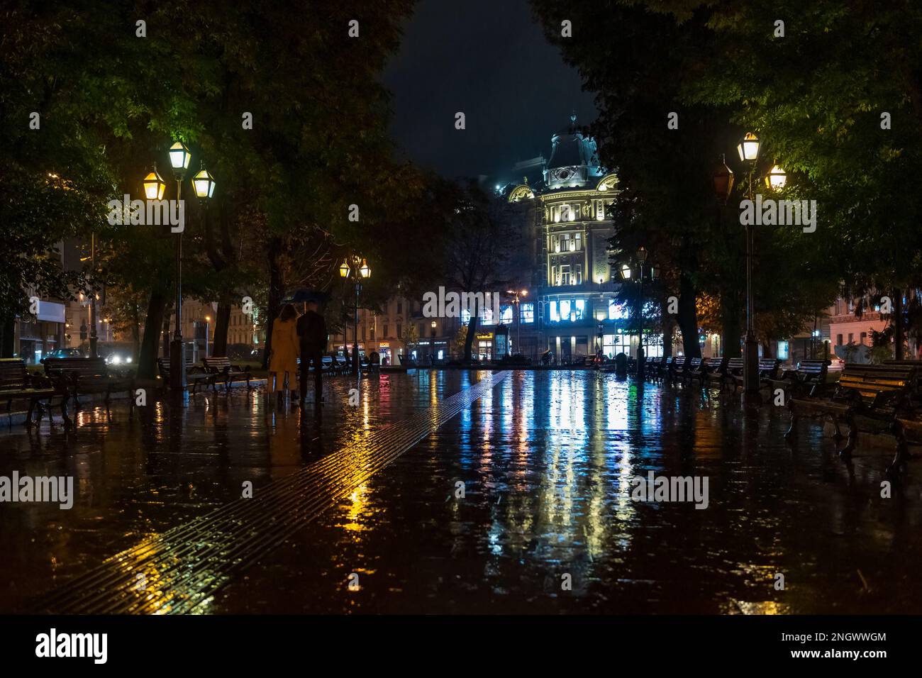 2020-09-29 Lviv, Ukraine. Night in the Lviv city. Wet cobblestone with city lights reflections. Pedestrians with umbrellas pass on the city streets Stock Photo