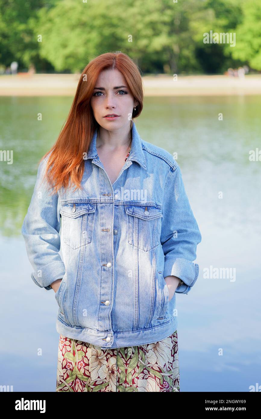 young woman wearing denim jacket over summer dress standing by lake - authentic real people Stock Photo