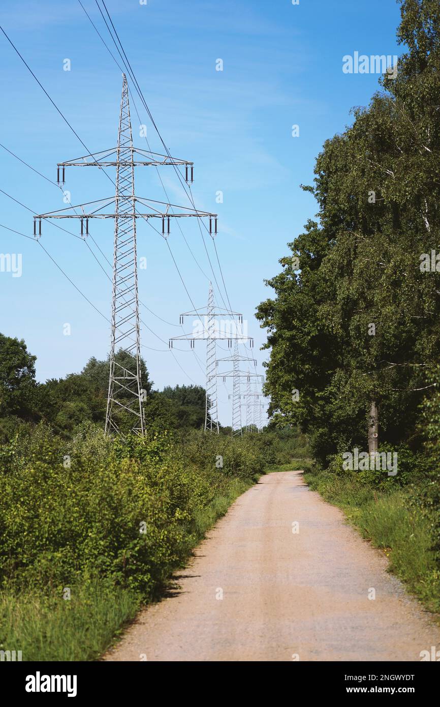 transmission line or overhead power cable with electricity pylons along rural dirt track country lane path through german countryside Stock Photo