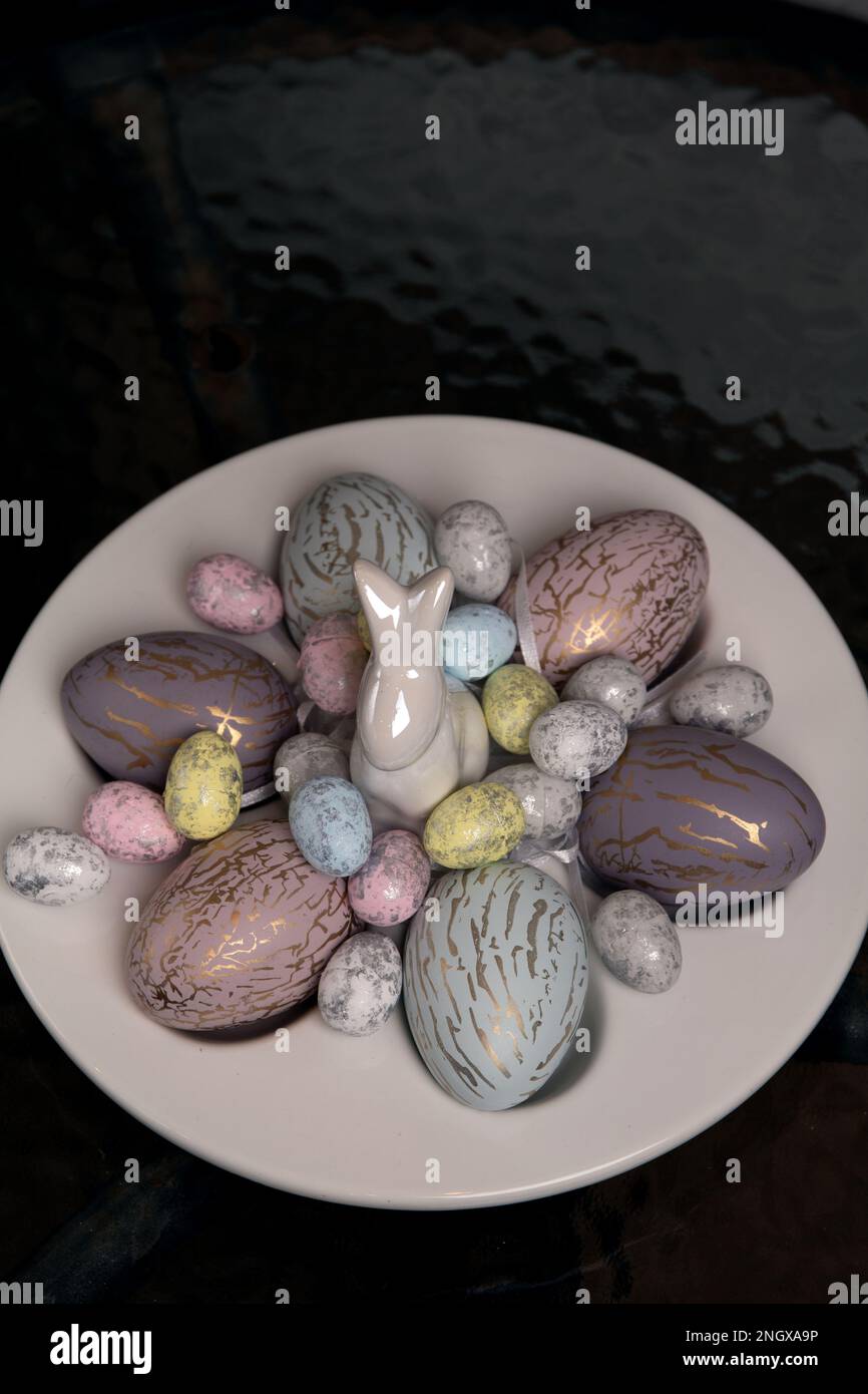 There are a lot of colorful photos lying on a white egg plate and a decorative rabbit on the table Stock Photo