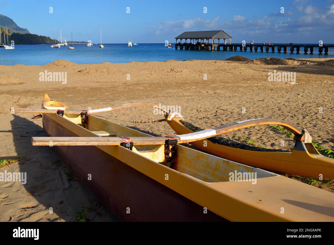 An outrigger rests on the sand of a tranquil beach on Hanalei Bay, Kauai, Hawaii Stock Photo