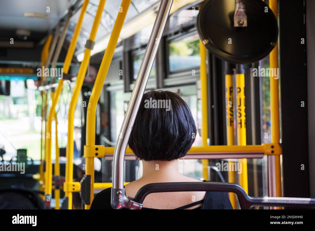 Toronto Transit passenger. Young woman alone in TTC bus sitting beside the line of handles. Toronto Transit Commission is public transport agency that Stock Photo