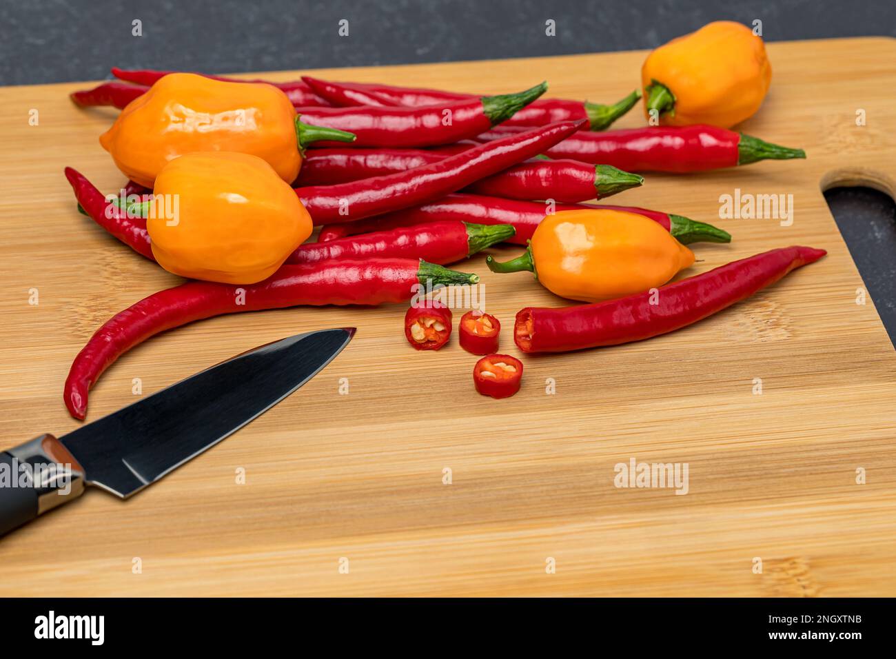 Slicing hot peppers on kitchen cutting board. Hot pepper farming, fresh and organic vegetables concept. Stock Photo