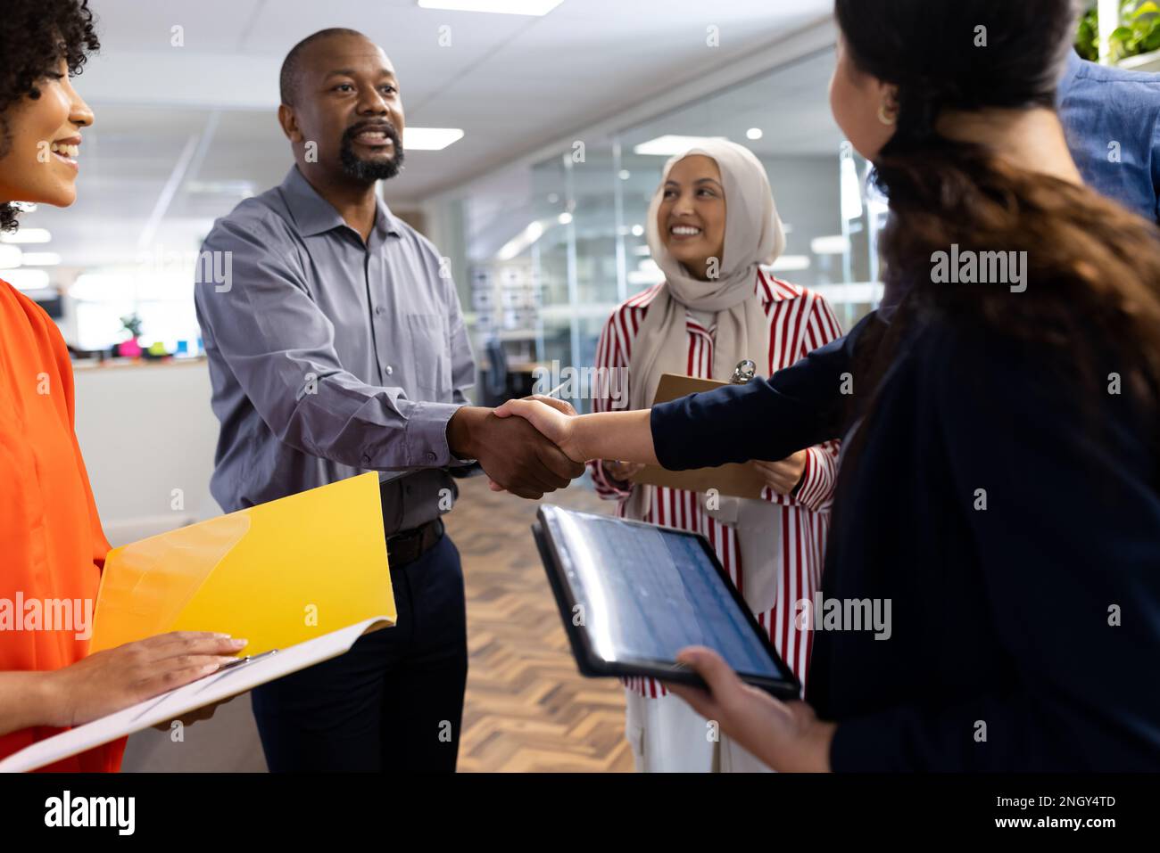 Happy diverse female and male businesspeople talking and shaking hands in office Stock Photo