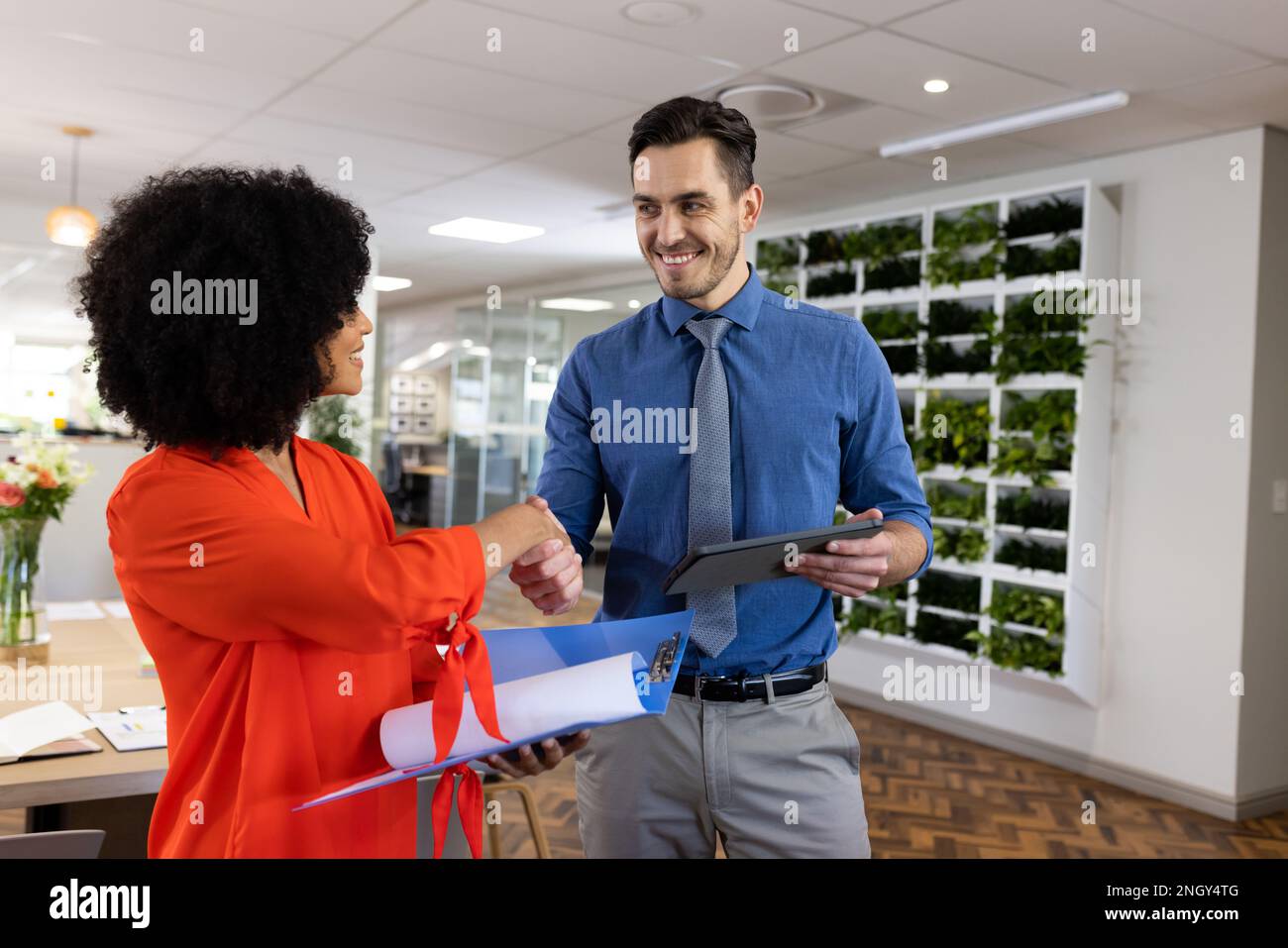 Diverse female and male businesspeople smiling and shaking hands in office Stock Photo