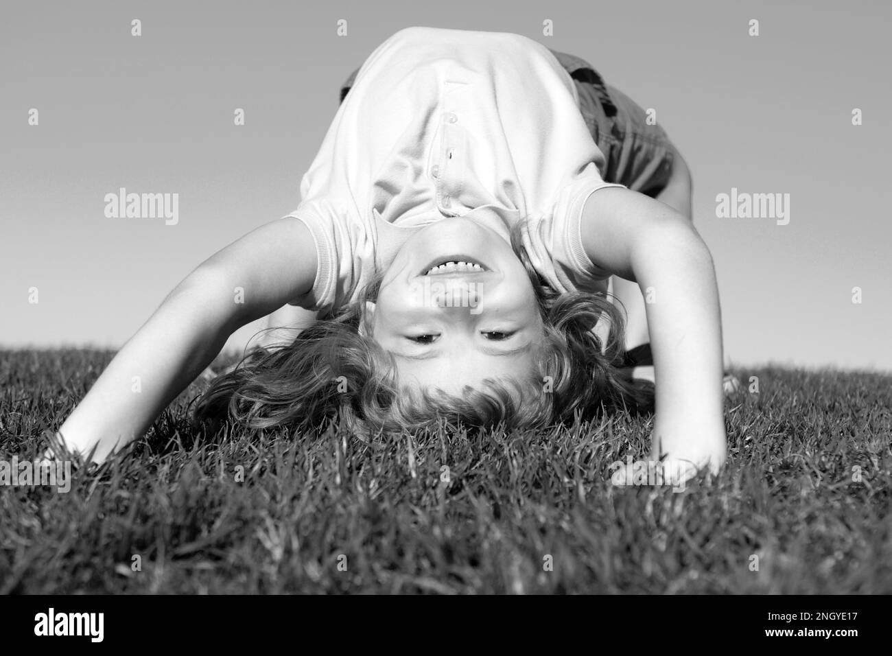 Portrait of a happy smiling child boy playing upside down on grass field outdoor. Laughing child. Expressive facial expressions. Stock Photo