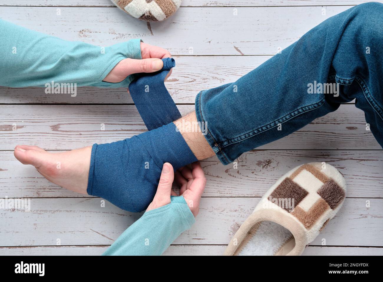 An adult wrapping compression bandage around sprained ankle of teenage