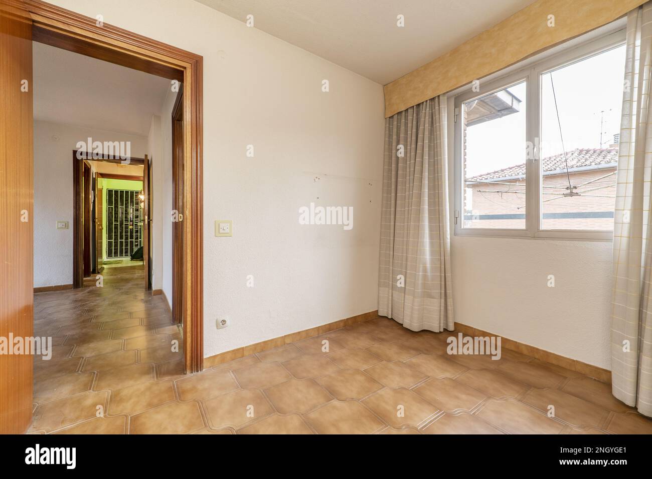 Empty room with brown stoneware floors, window with curtains and access door to other rooms Stock Photo