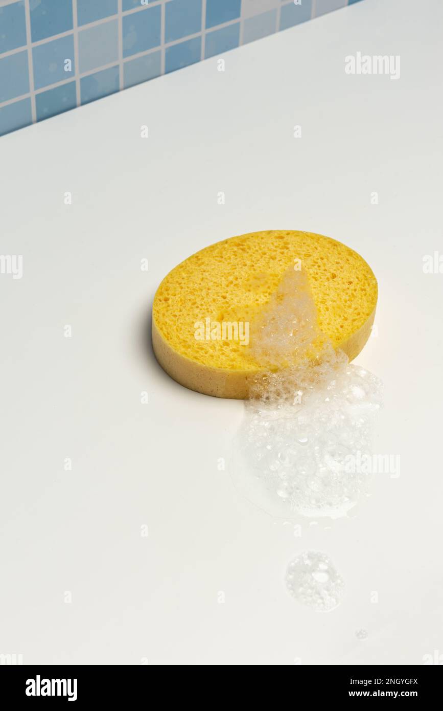 A yellow synthetic bath sponge with soap foam on a white surface Stock