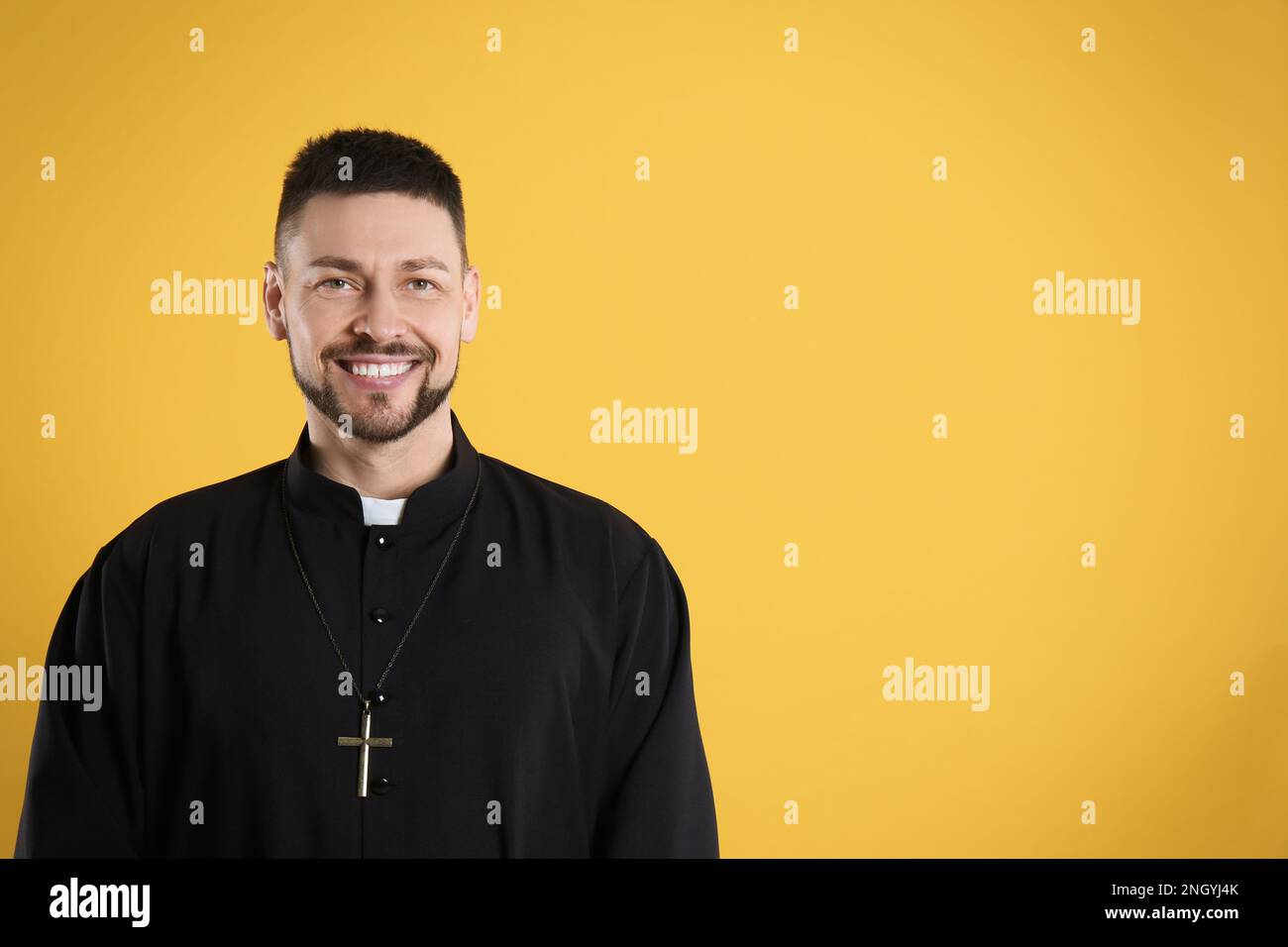 Priest wearing cassock with clerical collar on yellow background, space for text Stock Photo