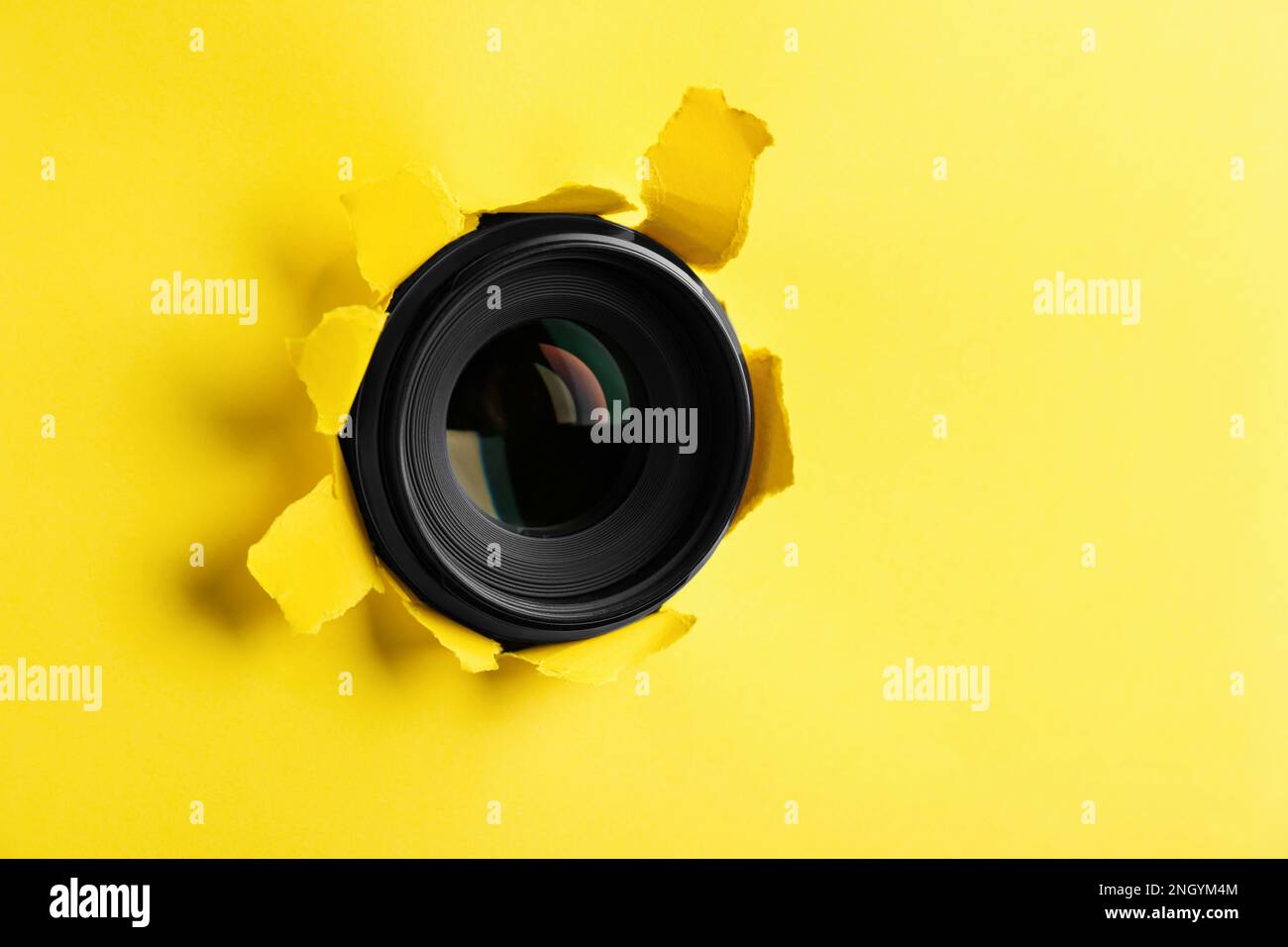 Hidden camera lens through hole in yellow paper Stock Photo Alamy