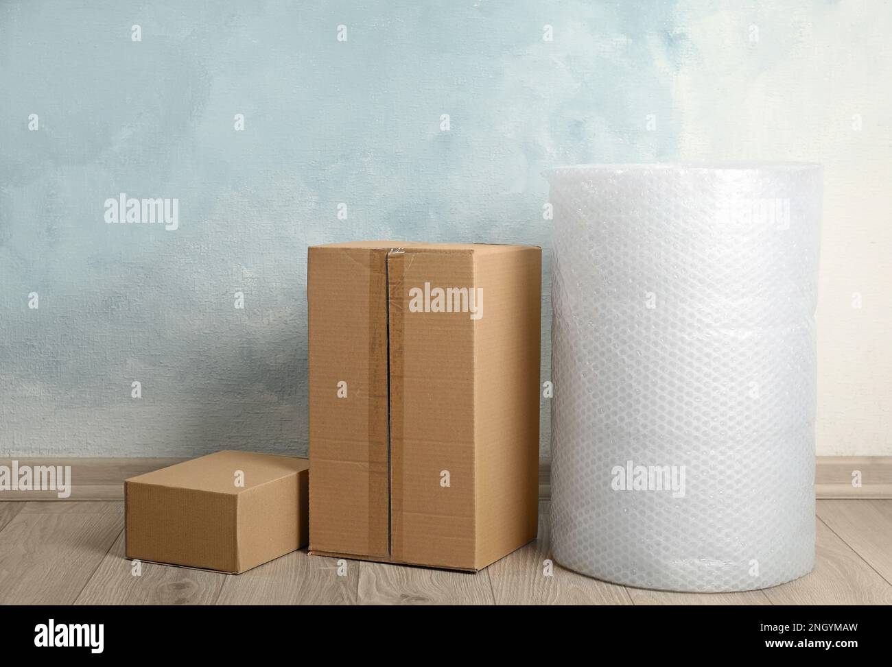 Bubble wrap roll and cardboard boxes on floor near light blue wall