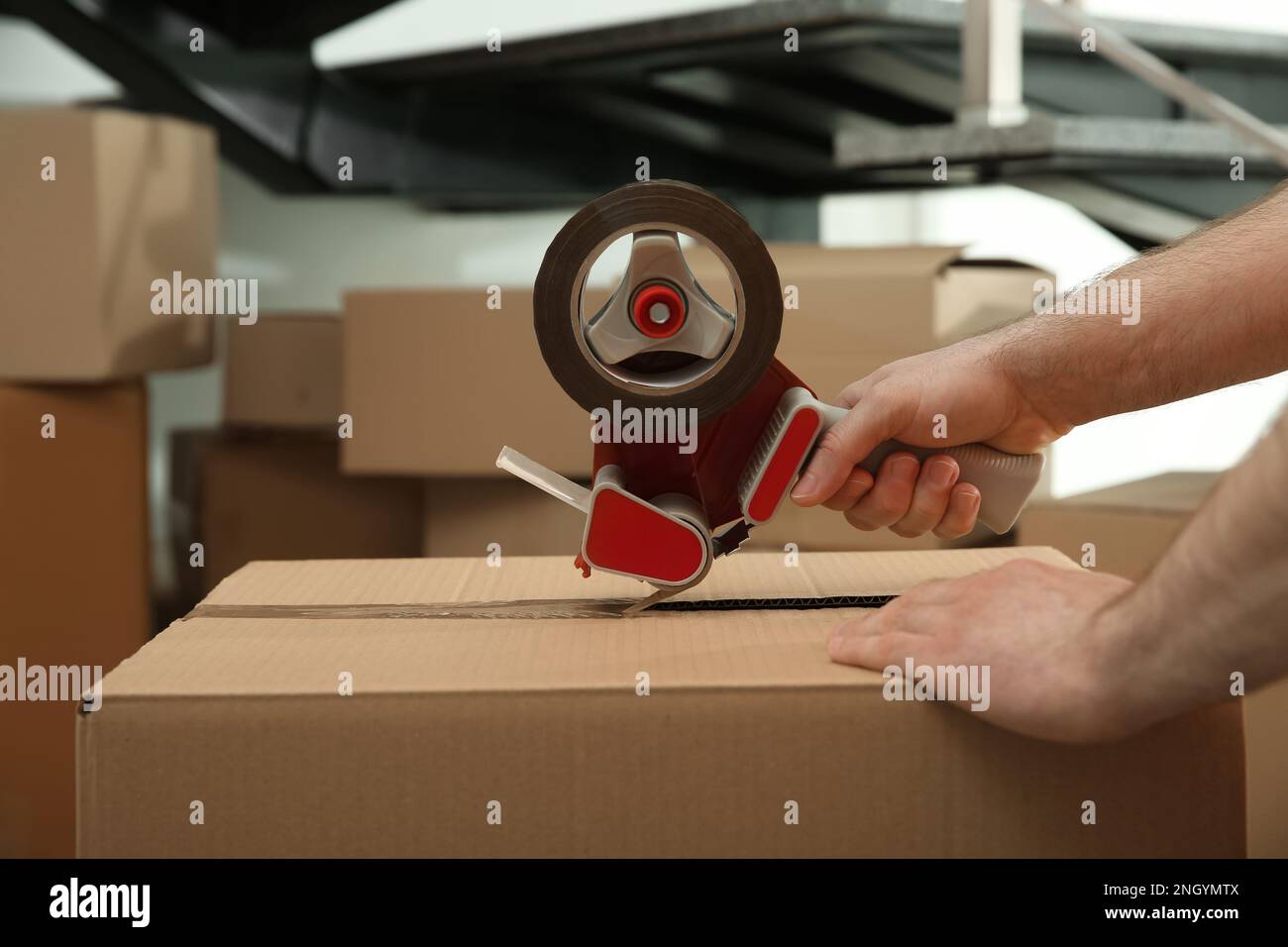 Worker taping cardboard box indoors, closeup view Stock Photo
