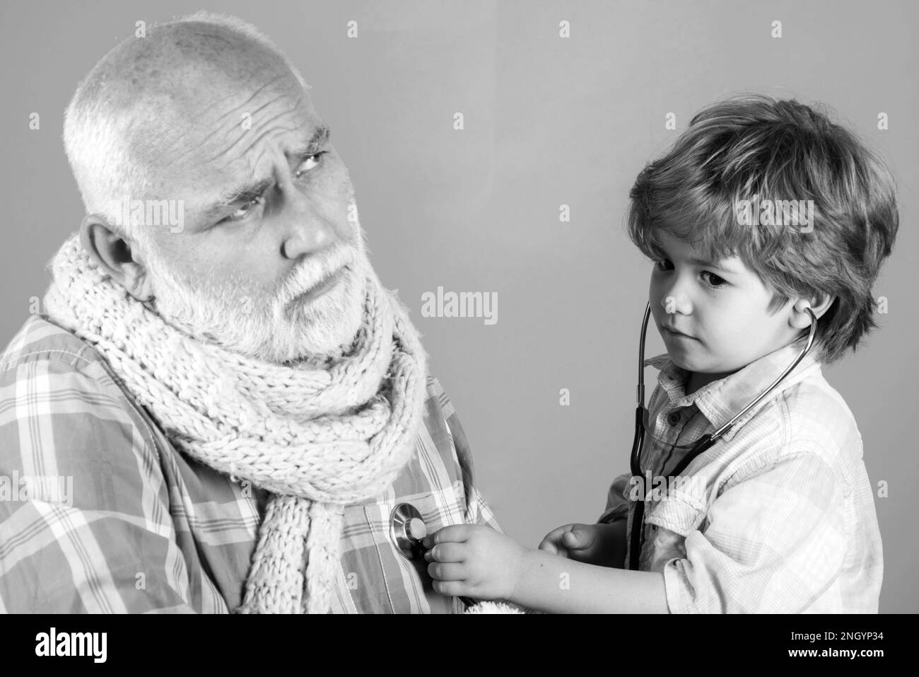Smiling little boy playing doctor and listening old grandfather with stethoscope. Little doctor. Boy in doctor uniform treat patient. Stock Photo