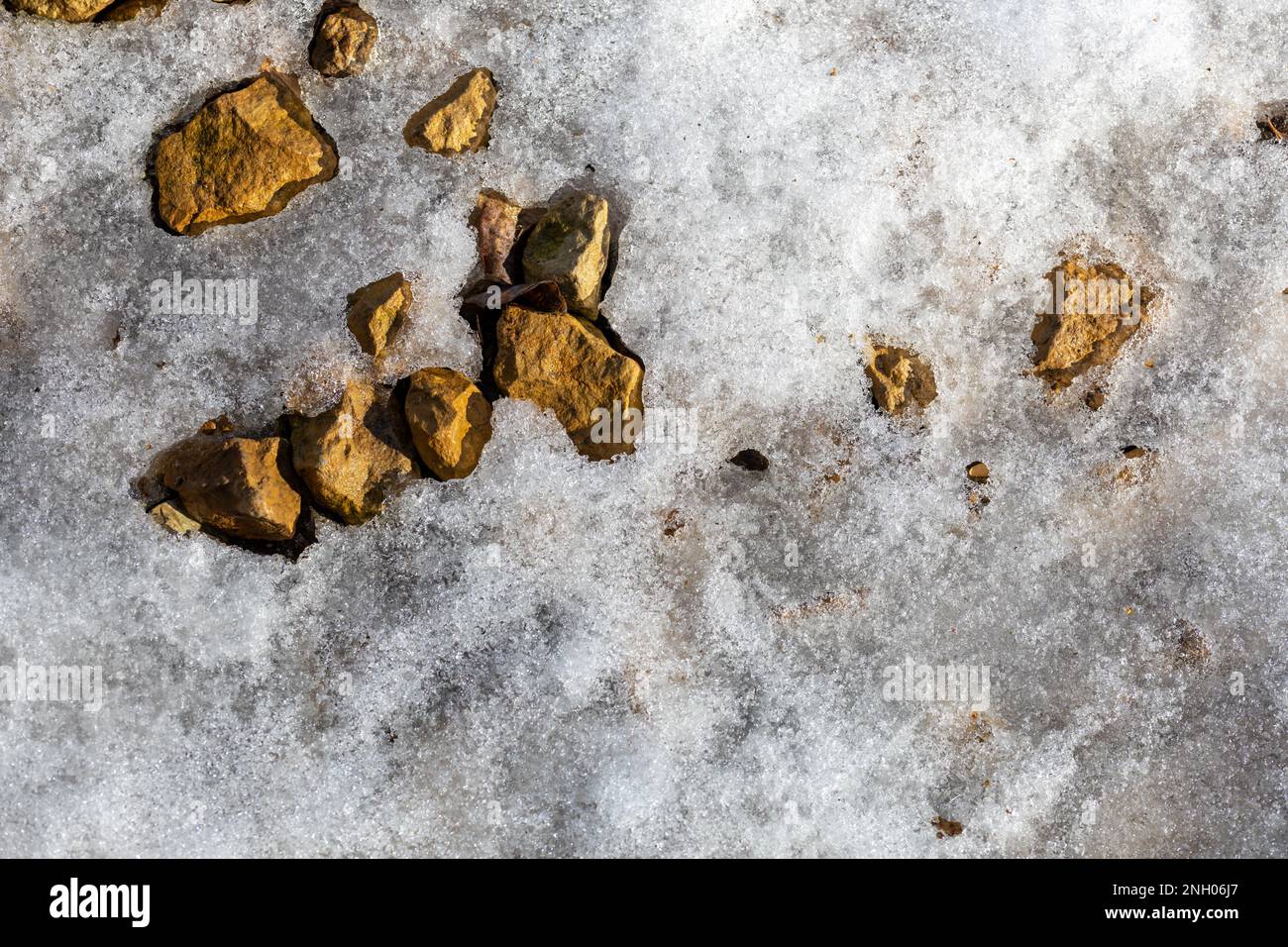 Full frame abstract texture background of snow beginning to melt under natural sunlight in late winter, exposing crushed rock under the surface Stock Photo