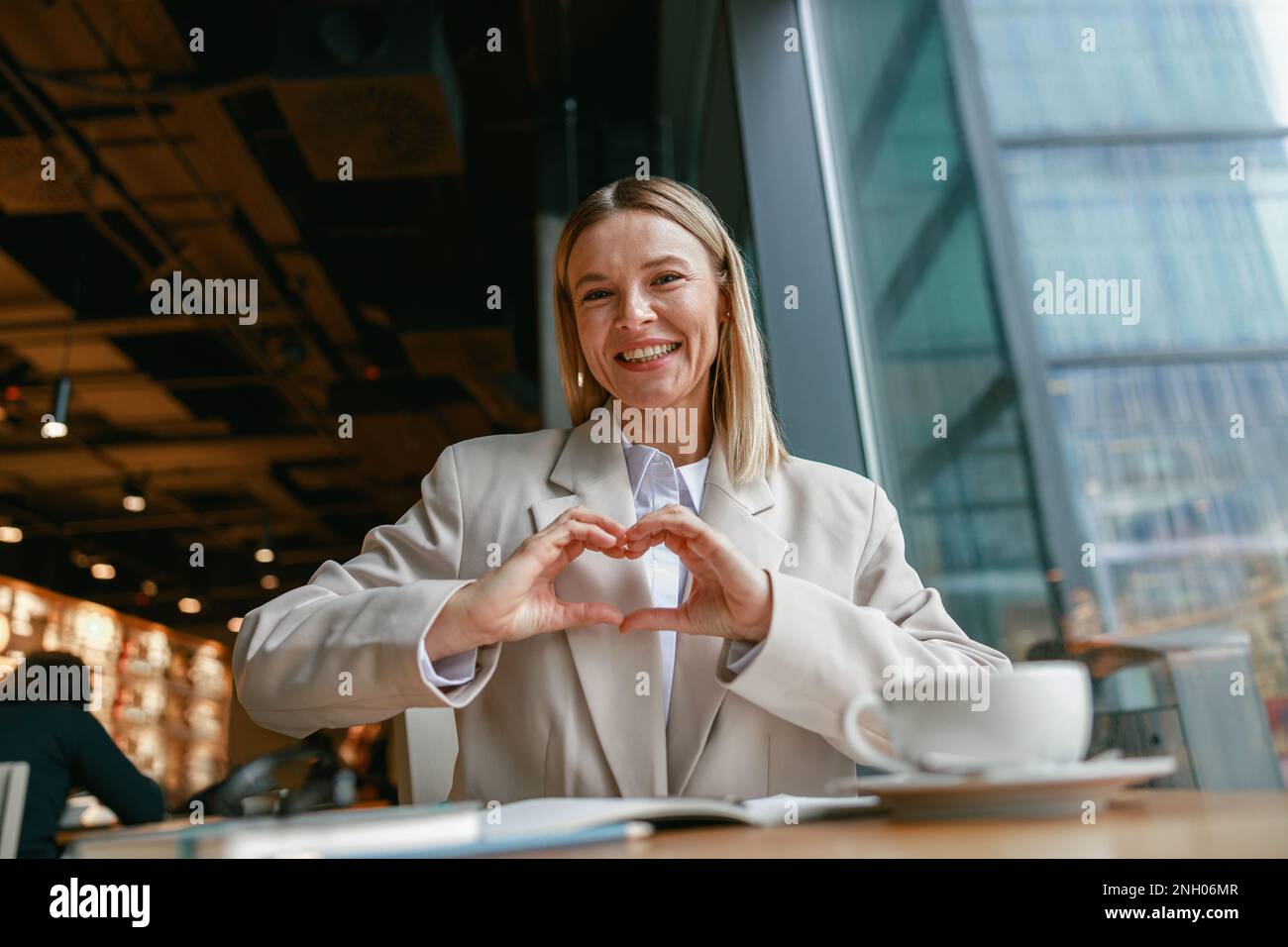 Smiling businesswoman showing heart shape with gesture while working in ...