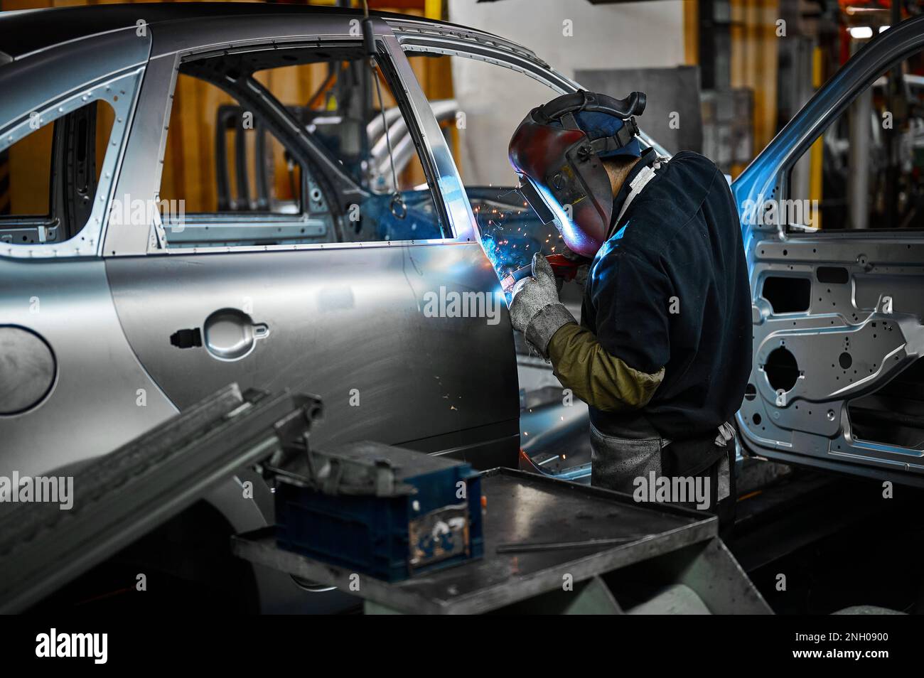 Worker in mask welds metal parts of auto carcass in shop Stock Photo