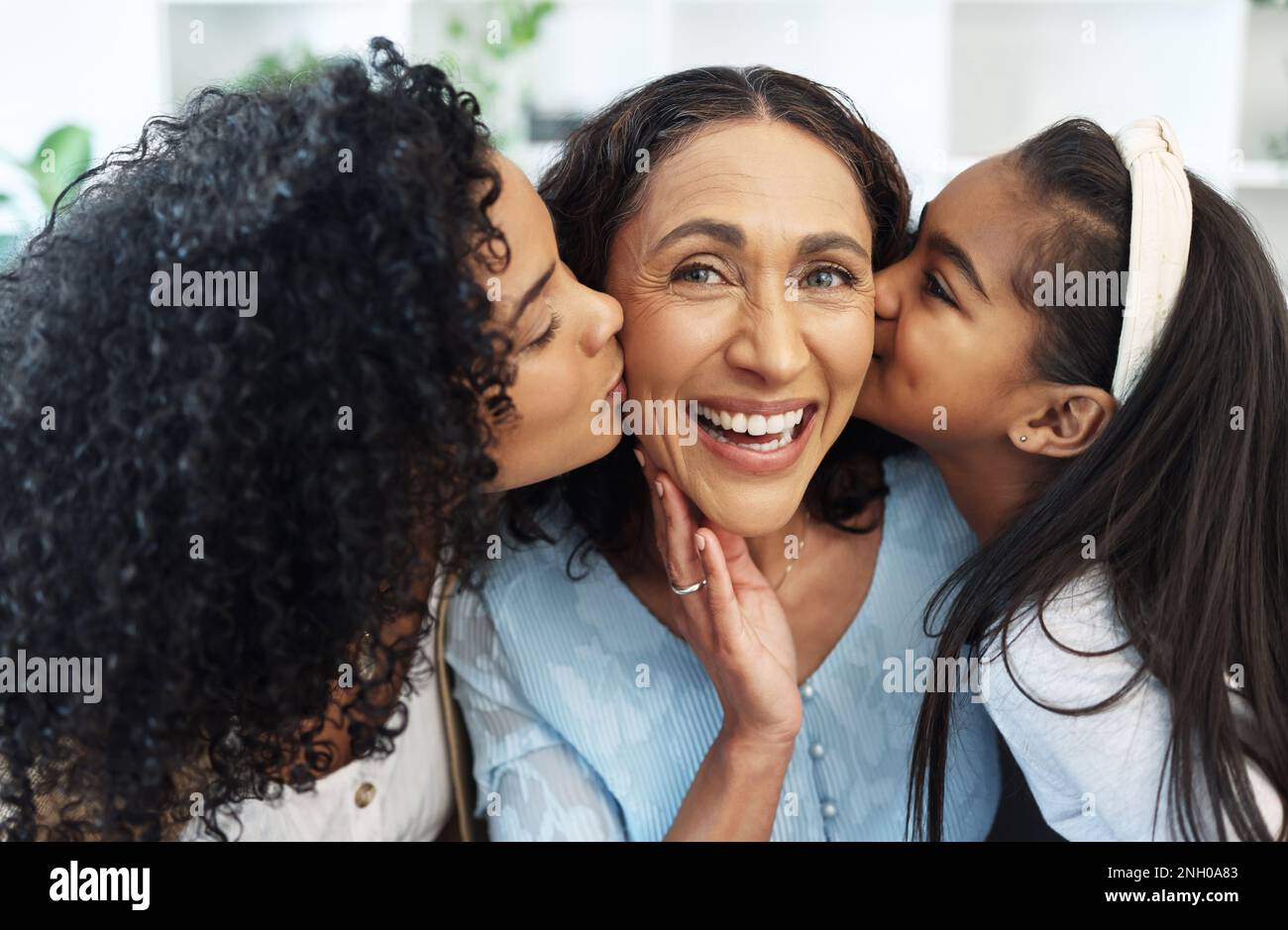 Portrait, cheek kiss and grandmother with family, daughter and granddaughter at home together. Face, love and care of happy mother, senior woman and Stock Photo