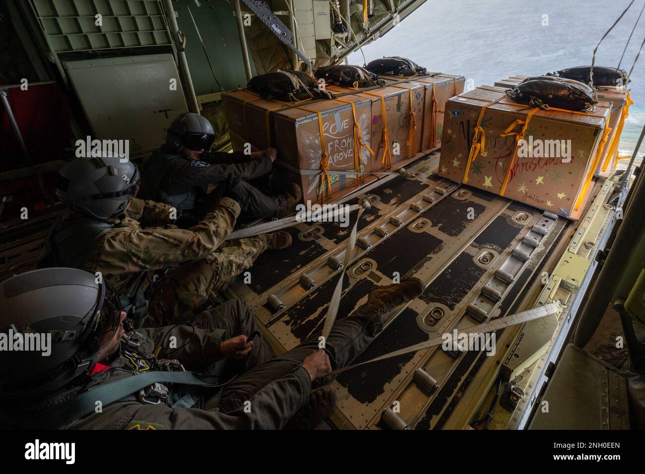 (Right to left) U.S. Air Force Airman 1st Class Cameron Palmer, Tech. Sgt. Ryan Berry, and Senior Airman Dakota Davis, 36th Expeditionary Airlift Squadron C-130J loadmaster, push bundles over Ulithi, Federated States of Micronesia, Dec. 4, 2022. The aircraft, call sign Santa 11, delivered 14 bundles to the eastern Caroline Islands, included Asor, Falalop, and Fais islands. OCD is the longest-running Department of Defense humanitarian and disaster relief mission. Each year, the USAF partners with countries in the Pacific Air Forces area of responsibility to deliver supplies to remote islands in Stock Photo